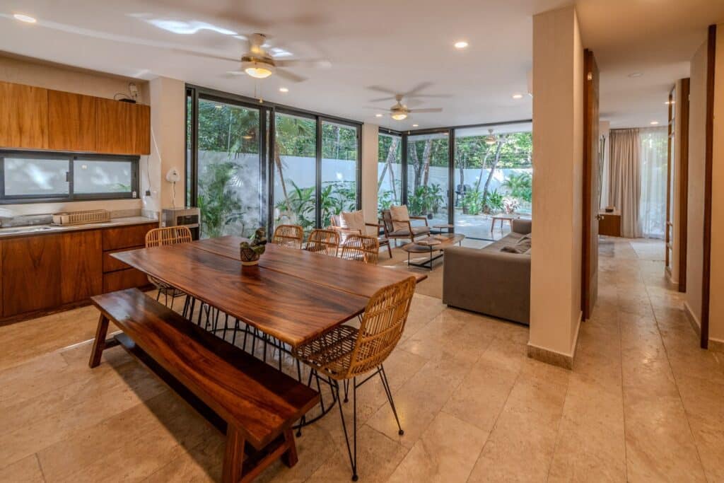 Living room with large glass sliding doors opening to lush outdoor garden area at Villa Las Almas in Aldea Zama, Tulum.