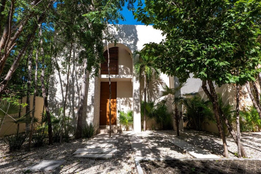 Modern house with wooden accents surrounded by lush trees and tropical plants at property at Villa Serenia in Kaybe Tulum.