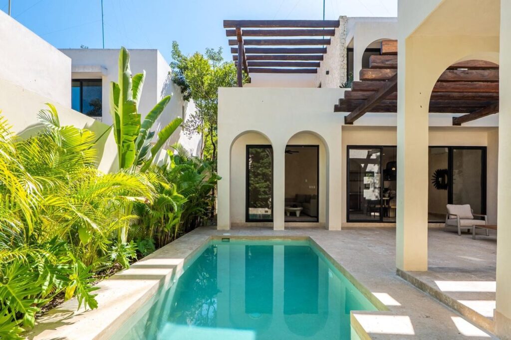 Outdoor view of a modern house with a swimming pool, surrounded by lush green plants at Kaybe Tulum at Villa Serenia.