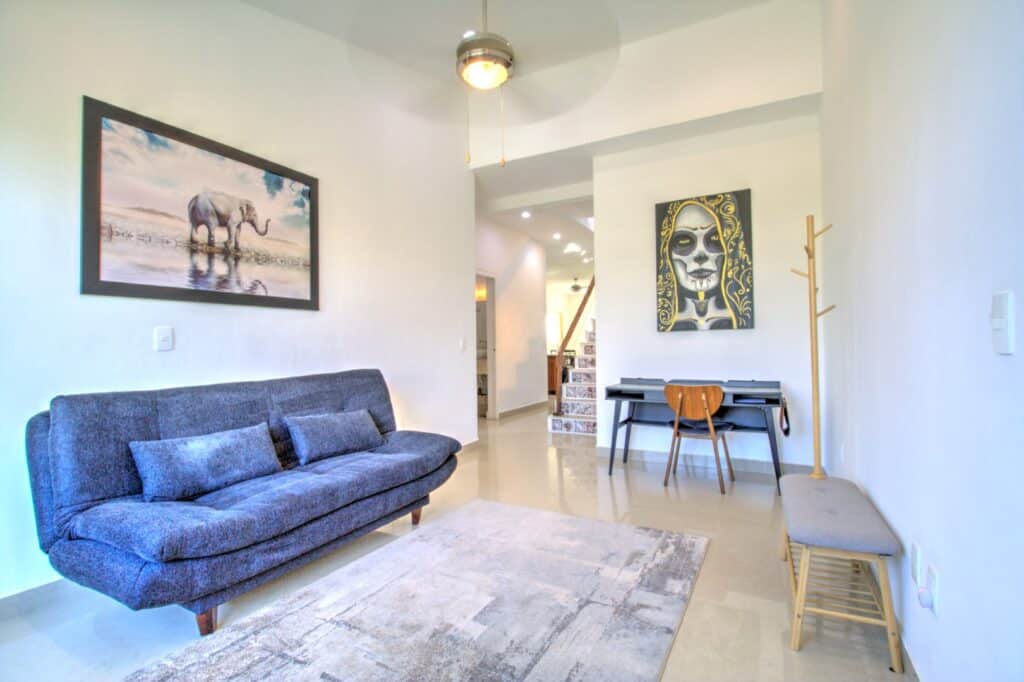 Interior of a living room with a blue sofa, wall art, a desk, and a staircase at property at Villas Aventuras Penthouse in Boulevard Puerto Aventuras.