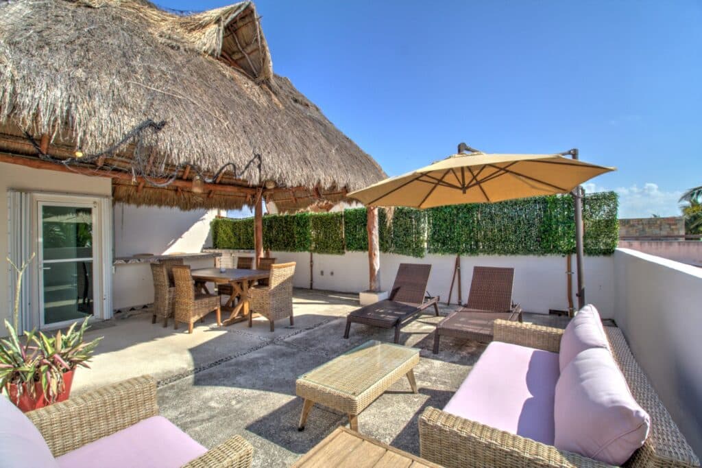 Sunlit rooftop terrace with wicker furniture, umbrellas, and potted plants, overlooking a clear sky at property at Villas Aventuras Penthouse in Boulevard Puerto Aventuras.