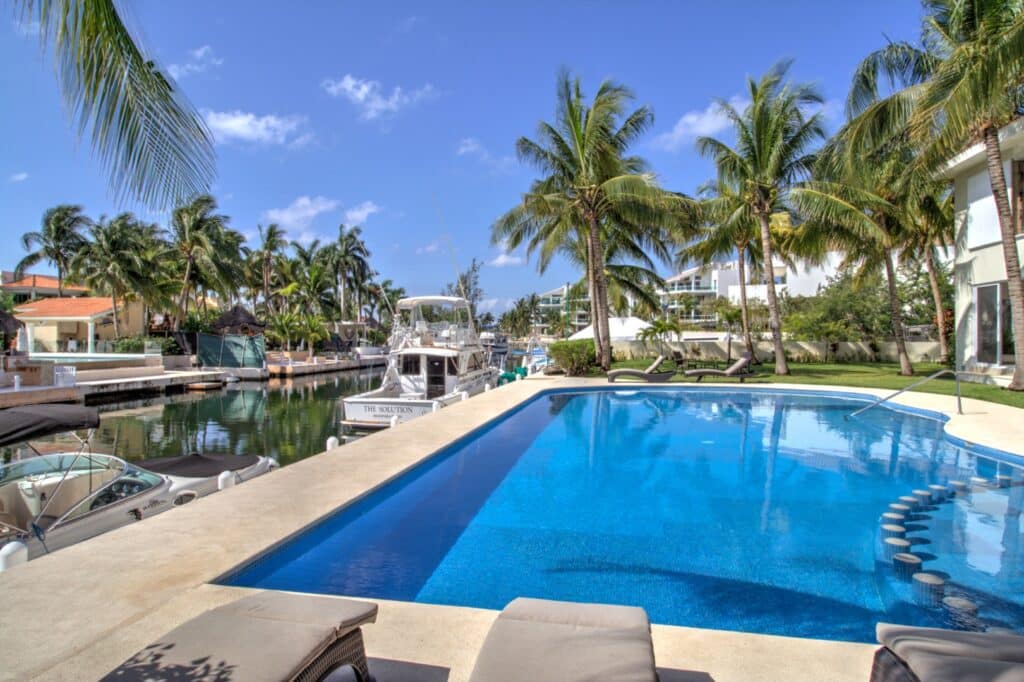 Swimming pool with seating area overlooking a canal with boats and palm trees on Boulevard Puerto Aventuras at Villas Aventuras Penthouse.