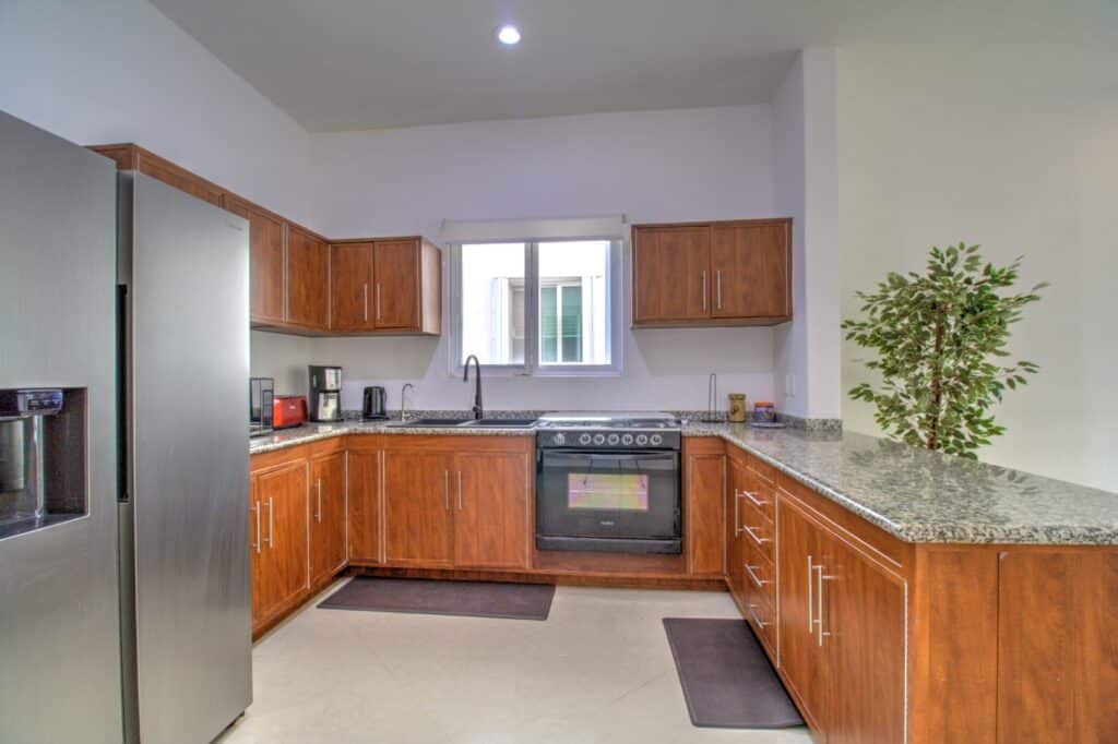 Modern kitchen with wooden cabinetry, stainless steel refrigerator, granite countertops, and a small window in Villa Aventuras Penthouse on Boulevard Puerto Aventuras.
