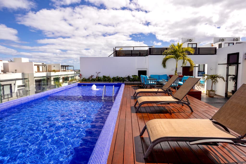 Rooftop terrace with a pool, lounge chairs, and outdoor seating under a cloudy sky at New Icono B407 condo at New Icono B407 3-Bedroom Condo in Playa del Carmen.