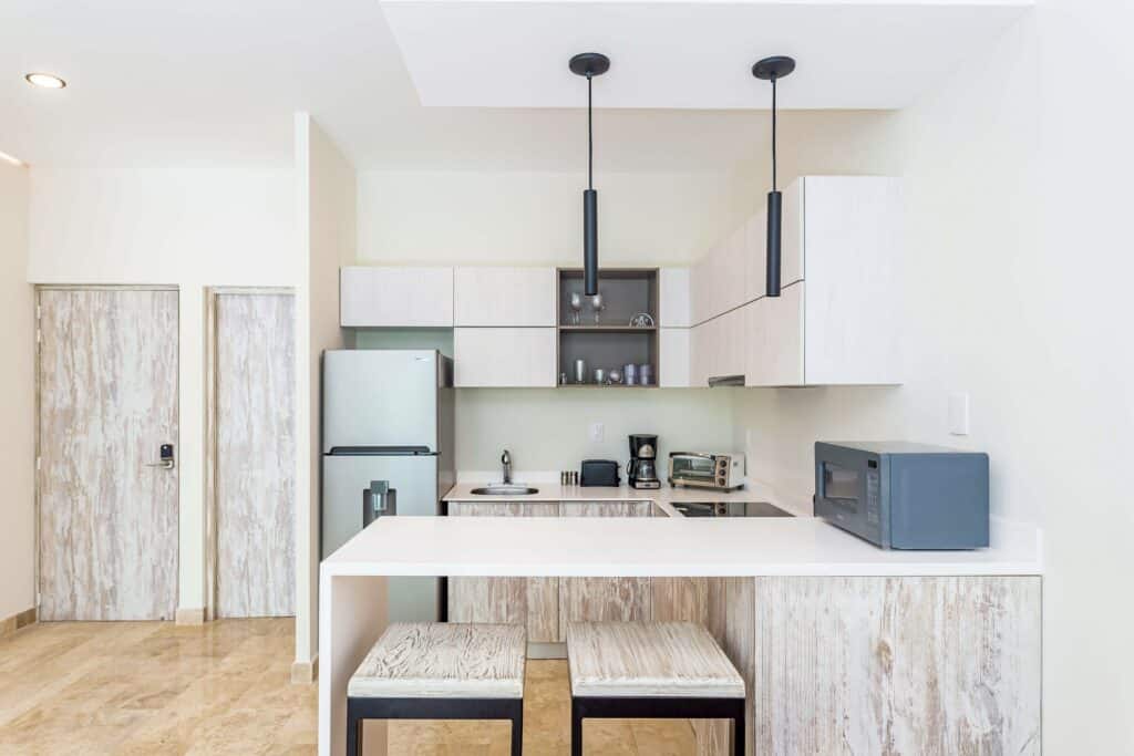 Modern kitchen with white cabinetry, black pendant lights, and small appliances, open to a dining area in Tulum at The Elle.