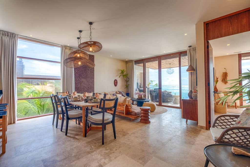 Interior view of a living and dining area with large windows overlooking a beach view in Tulum at Kaoba.