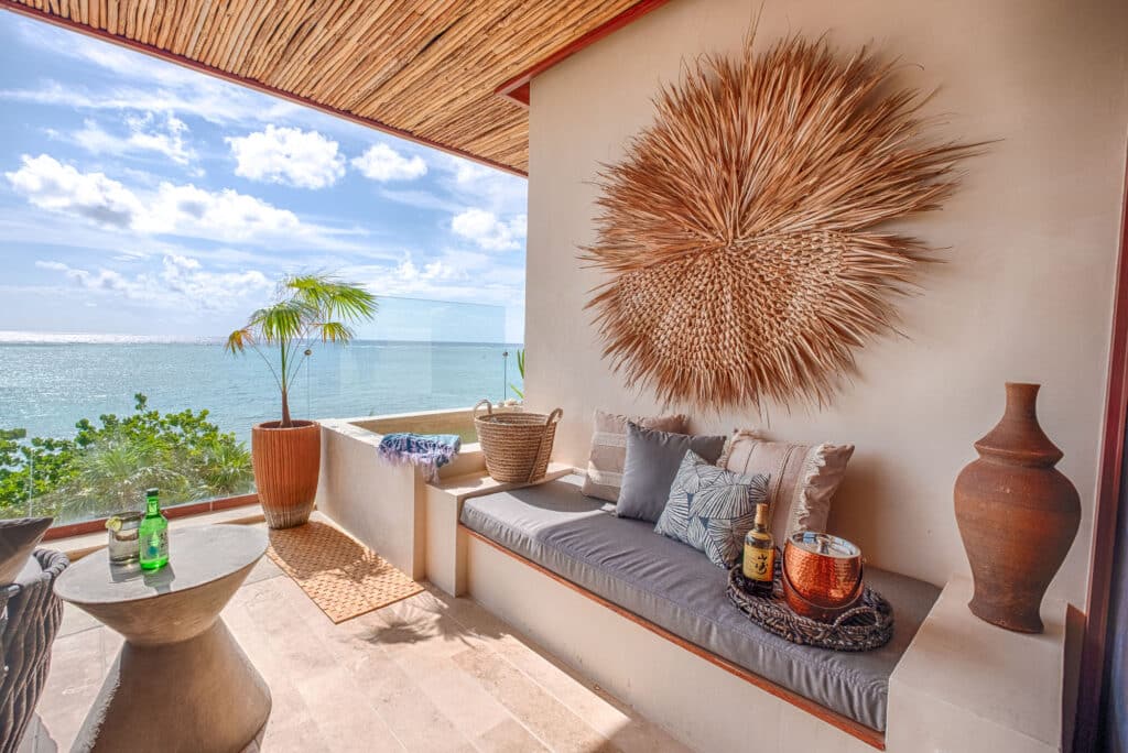 Balcony overlooking the ocean with woven wall art, potted plants, and cozy seating in Tulum at Kaoba.