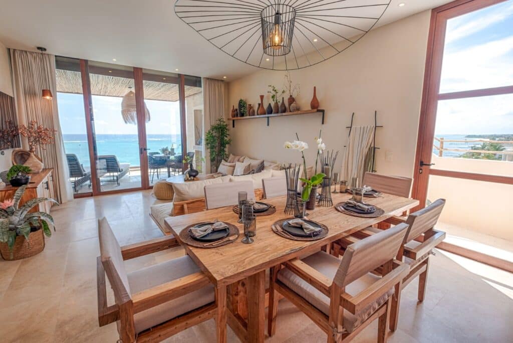 Living room with large glass doors opening to ocean views and a balcony, decorated in neutral tones with wooden accents and modern lighting at Kaoba in Tankah Bay, Tulum.