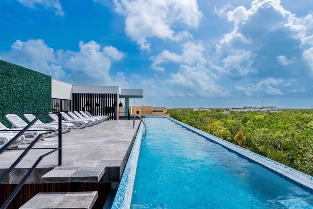 Swimming pool with lounge chairs overlooking a lush green landscape and partly cloudy blue sky in Tulum at The Elle.