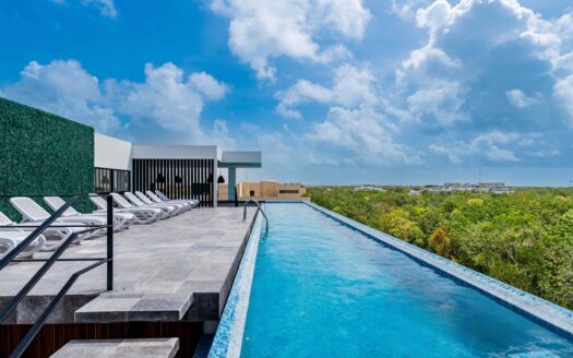 Swimming pool with lounge chairs overlooking a lush green landscape and partly cloudy blue sky in Tulum at The Elle.