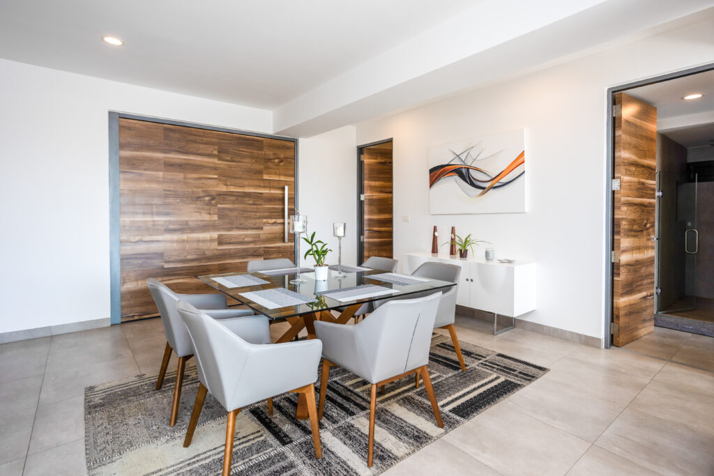Modern dining room with white chairs, wooden table, abstract art, and sliding wooden doors at Playa del Carmen property at New Icono B407 3-Bedroom Condo.