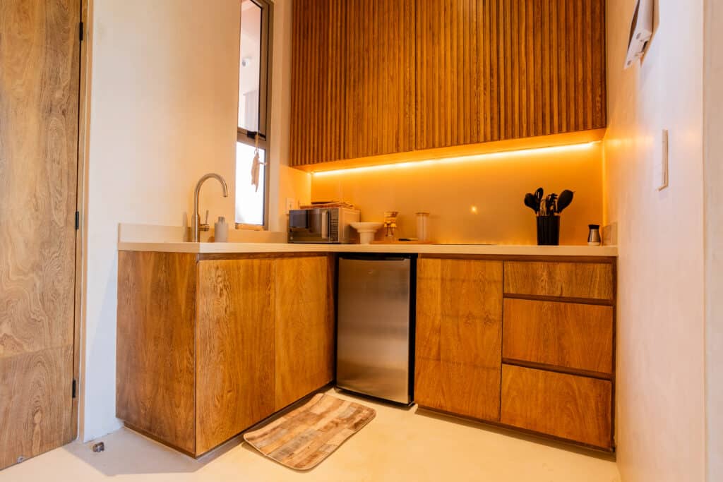 Modern kitchen with wooden cabinets, small refrigerator, microwave, and a window in Aldea Zama, Tulum, seen from a slightly tilted angle at Aflora.