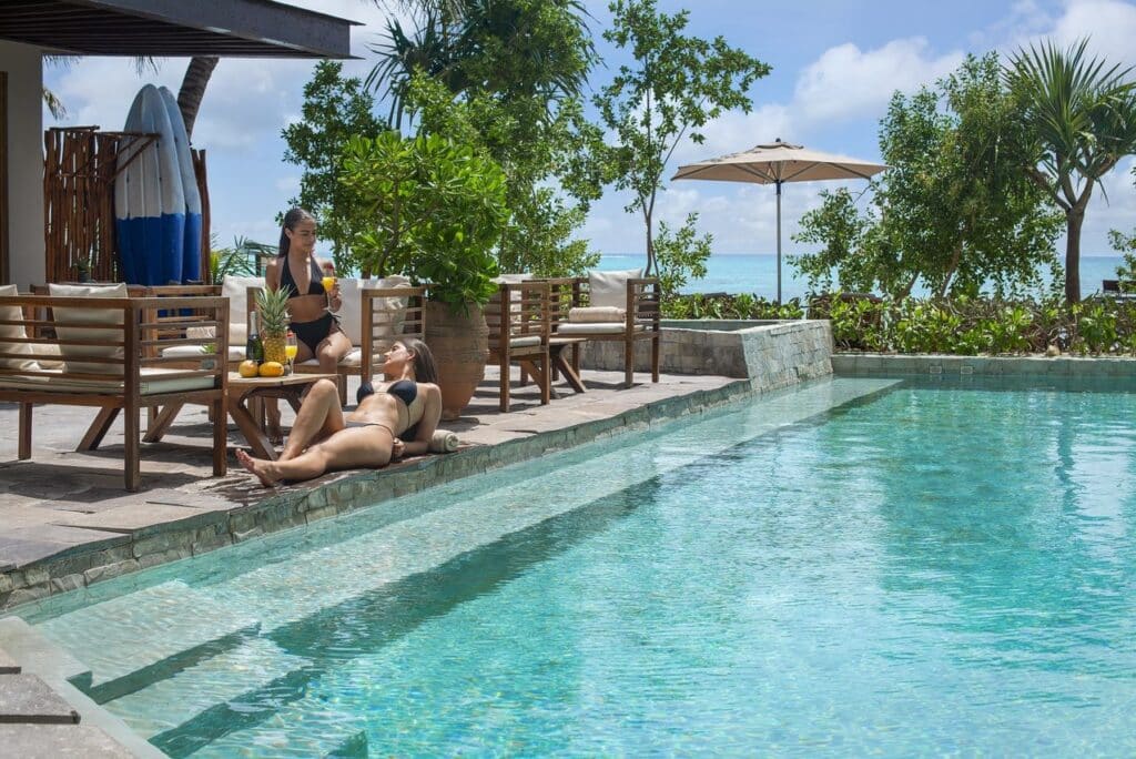 Two women relax by a poolside seating area overlooking a tropical landscape with ocean in the background in Tulum at 21 Room Hotel.