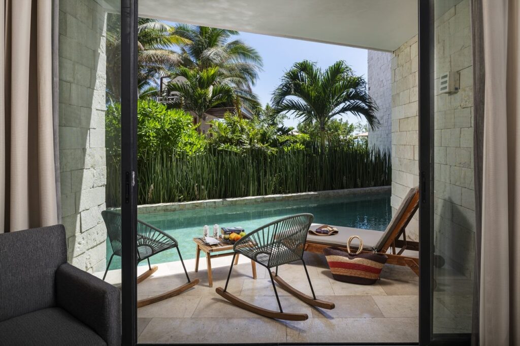 View from inside a room looking out to a private pool with lush tropical plants and palm trees in Tulum, Mexico at 21 Room Hotel.