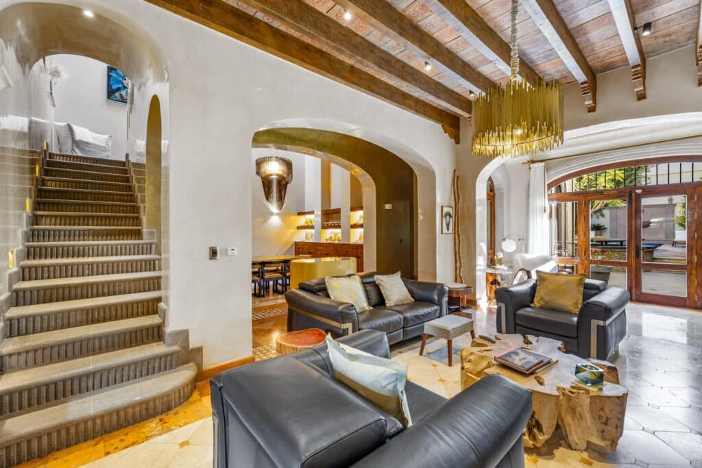 Interior of a spacious living room with high wooden beamed ceiling, modern black leather sofas, and large glass doors opening to an outdoor patio in San Miguel de Allende.