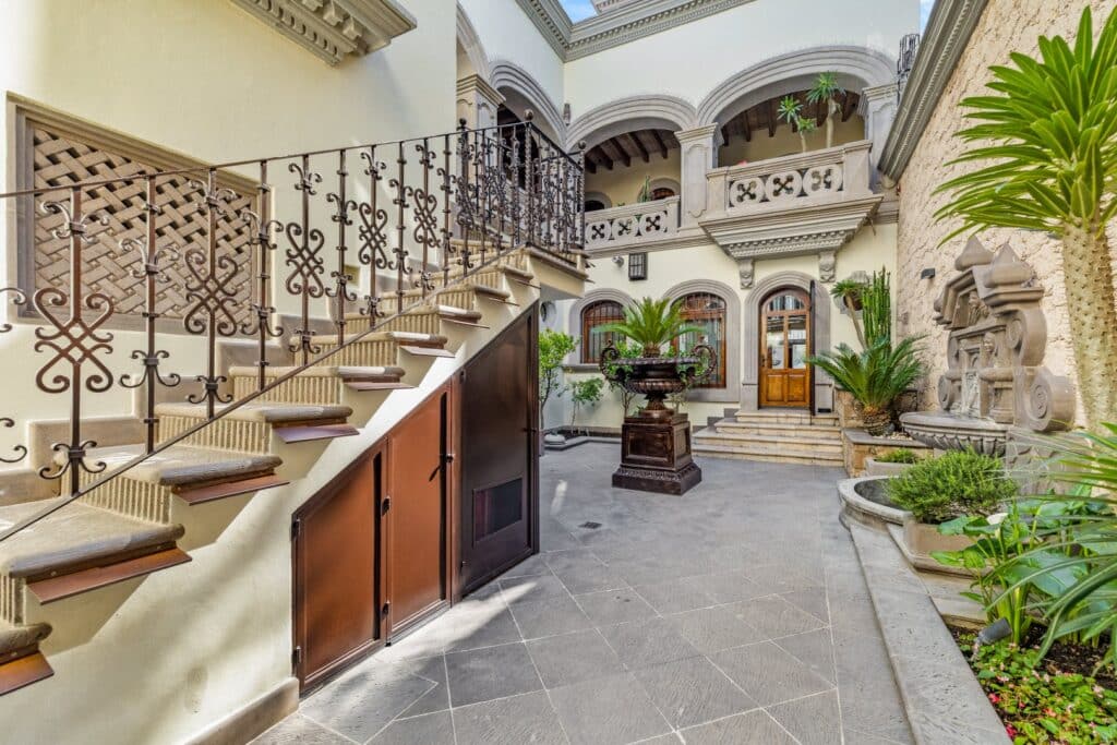 Interior courtyard with stairs, ornate railing, arched windows, potted plants, and historic architectural details at Casa 28 De Abril in San Miguel de Allende.