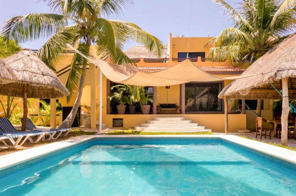 View of Casa Leo House 4 with swimming pool, palm trees, and shaded outdoor seating area at property at Casa Tankah Villa in Tankah Bay, Tulum.