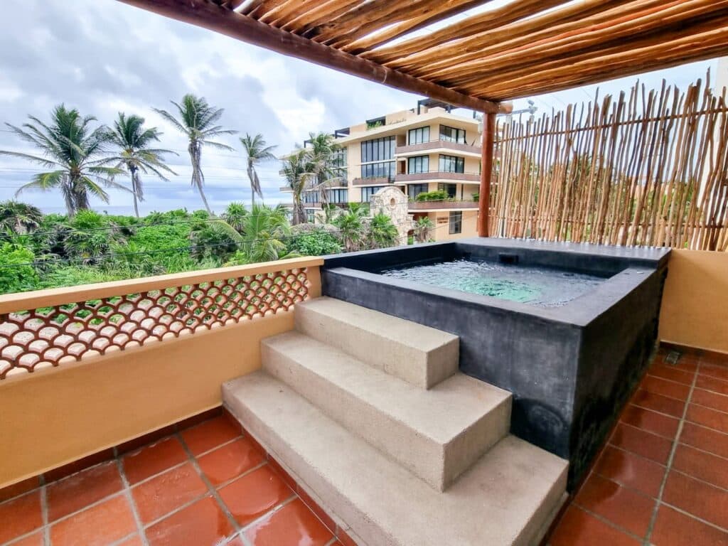 Balcony with a hot tub overlooking tropical greenery and neighboring buildings in Tulum at Casa Tankah Villa.