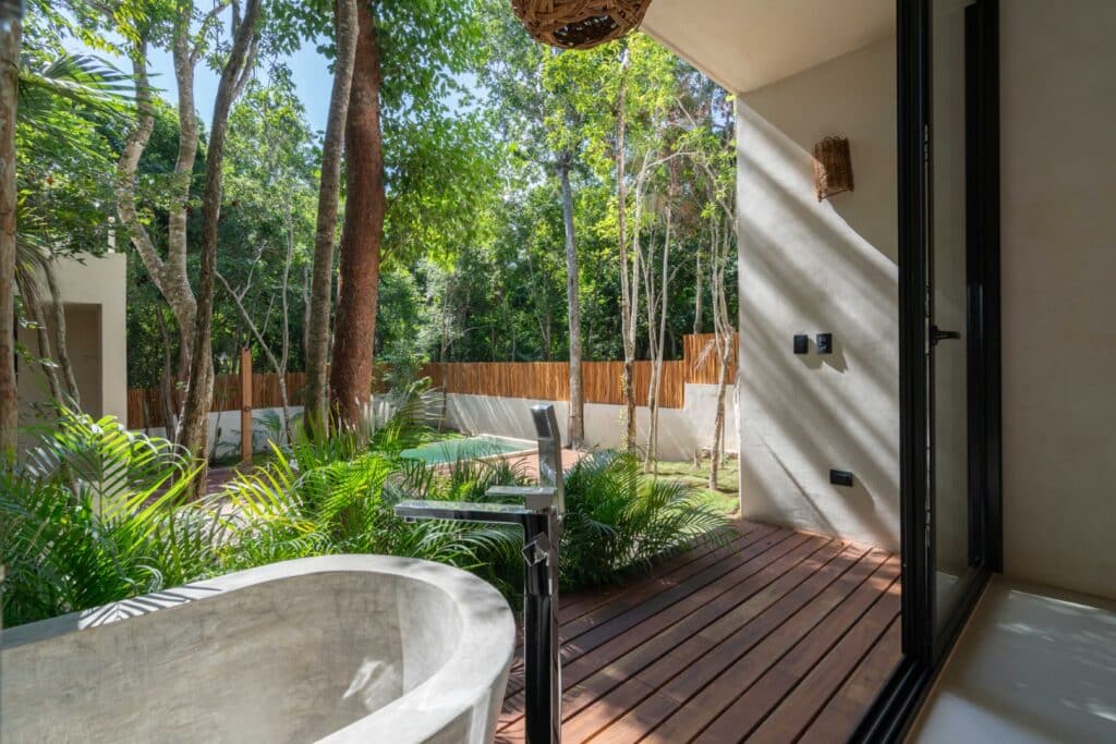 View from a patio featuring a stone bathtub, lush green trees, and a wooden deck at Zapote in Tulum.
