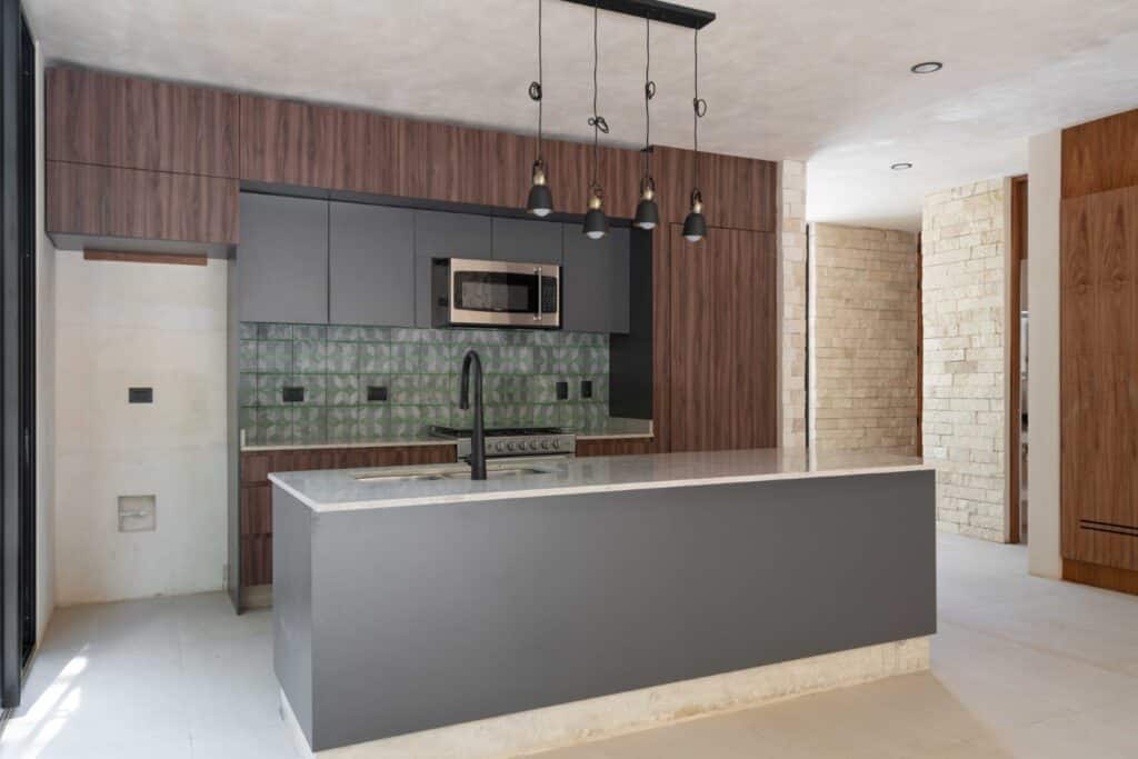 Modern kitchen with gray cabinets, black fixtures, colorful geometric backsplash, and a white stone island in a Tulum property at Zapote.