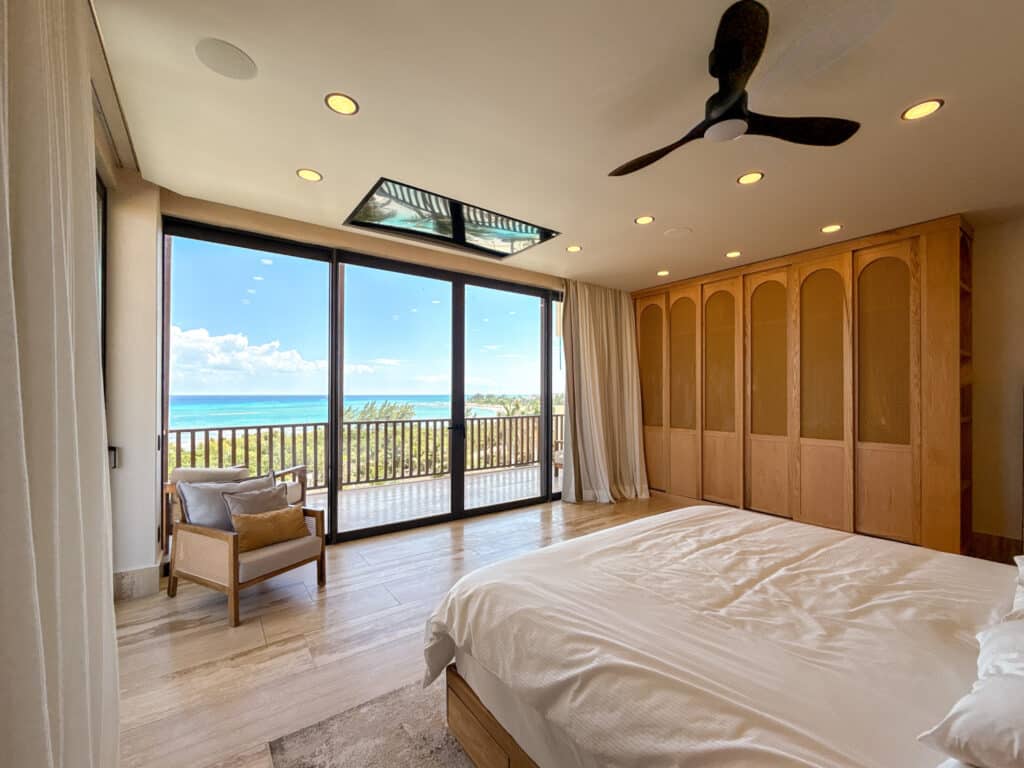 Bedroom with large sliding glass doors opening to a balcony with ocean view, wooden closet, and light-colored flooring in Costa Beach, Playa del Carmen.