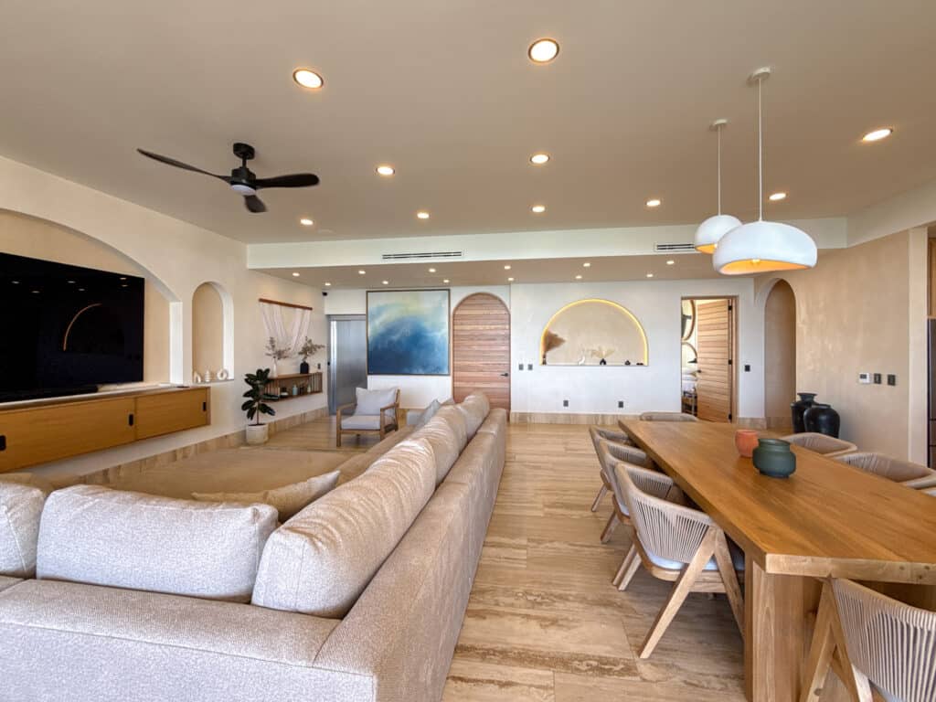 Modern living room with beige sectional sofa, wooden dining table, white pendant lamps, and decorative accents in neutral tones, Playa del Carmen at Costa Beach.