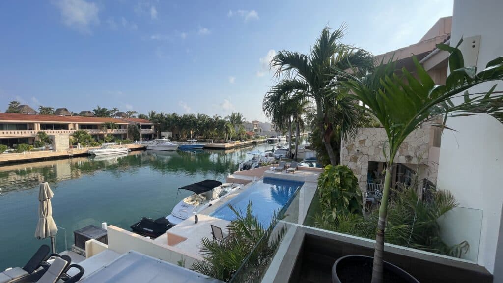 View of a marina with boats and a pool on a terrace, with palm trees and modern buildings nearby at Puerto Aventuras at Regatta 4 4-Bedroom Penthouse.