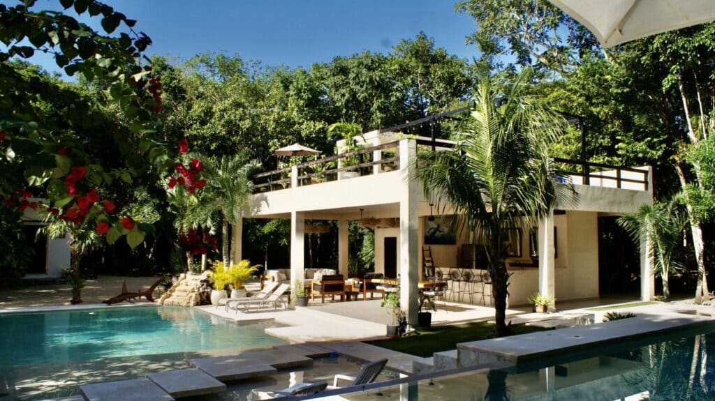 Modern two-story house with an outdoor pool surrounded by lush greenery at Hacienda MVO in Akumal.