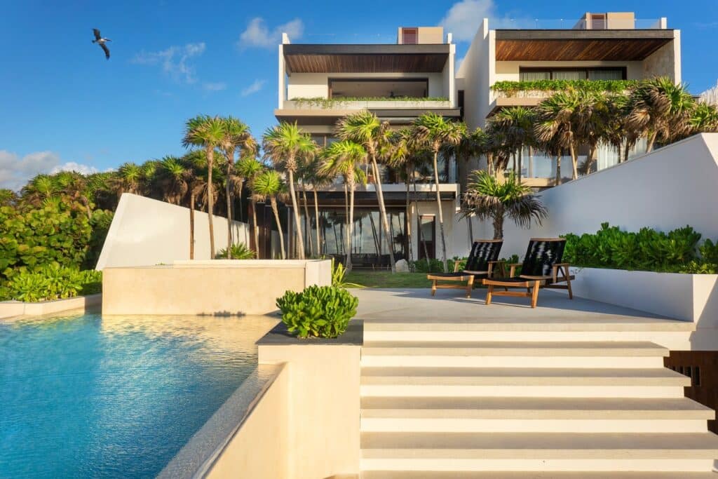 Modern beachfront house with pool, surrounded by lush tropical plants, overlooking clear blue sky and water at Casa Alina in Tulum.