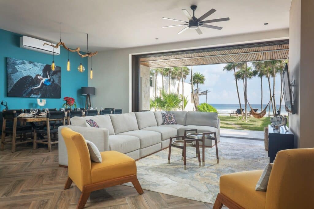 Living room with large glass doors opening to beachfront view of palm trees, hammock, and ocean at Casa Alina in Tulum.