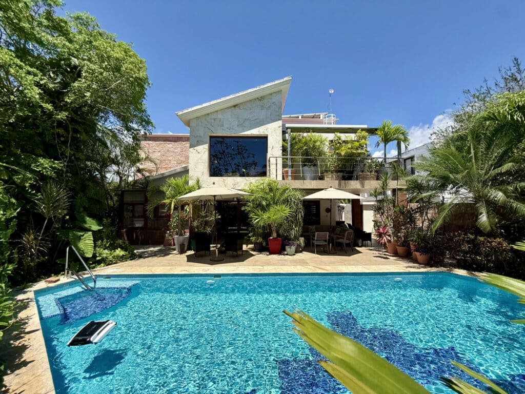 Modern house in El Cielo features a backyard with a swimming pool surrounded by lush tropical plants and outdoor seating areas at Casa Noyes.