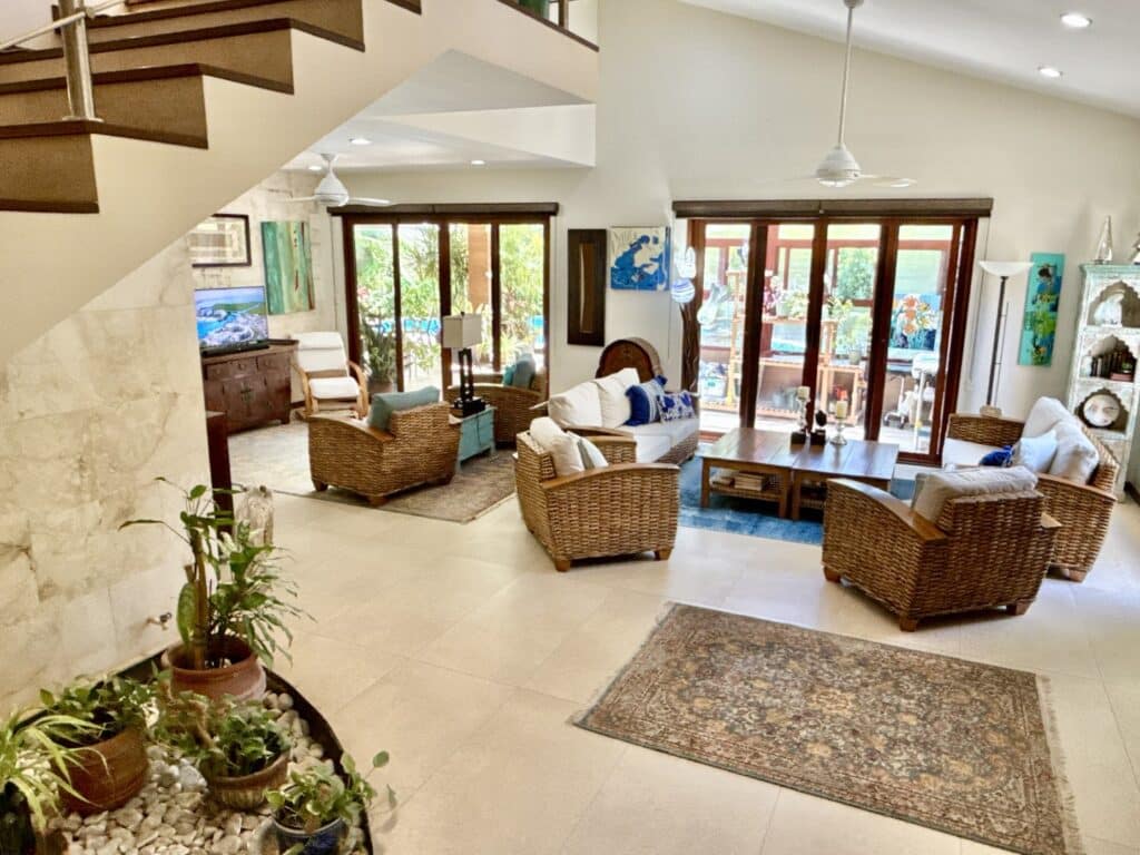 Living room with wicker armchairs, sliding glass doors, and colorful artwork, opening to a garden and patio in Playa del Carmen at Casa Noyes.