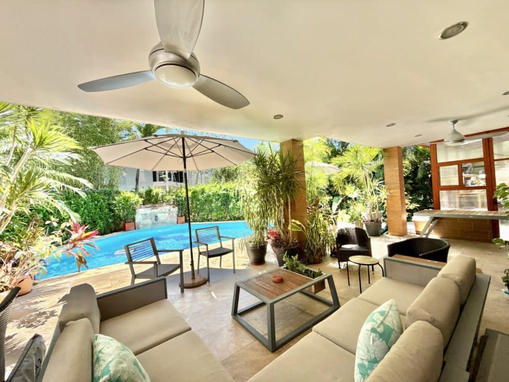 Covered outdoor patio with seating, lush plants, and a blue swimming pool in Playa del Carmen, Mexico at Casa Noyes.
