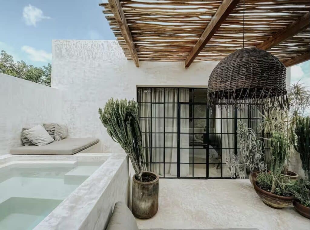 Terrace with a hot tub, outdoor seating, potted cacti and a woven pendant light, overlooking a bright, minimalist exterior wall with greenery at Canopia in La Veleta, Tulum.