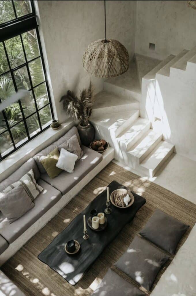 Living room with beige sofa, black coffee table, and large window with black grid framing views of greenery in Tulum at Canopia.