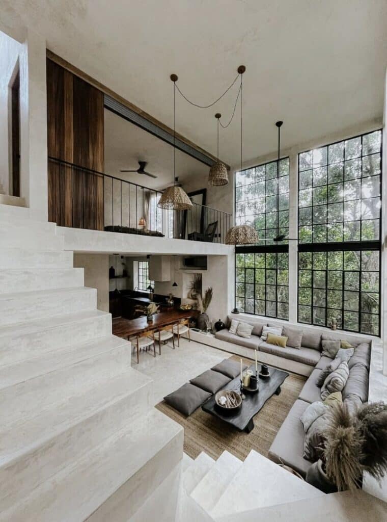 Open-concept living room with a high ceiling, large black-framed windows, and a sectional sofa in a modern Tulum home at Canopia.
