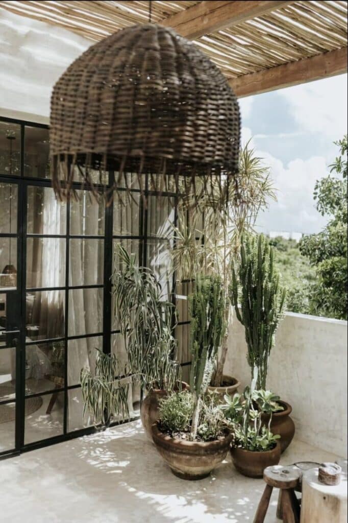Terrace with potted cactus and plants, wooden light fixture, and glass door leading inside in Tulum at Canopia.