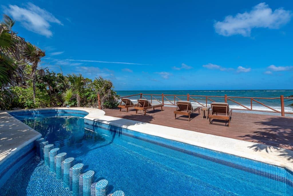 Beachfront view with wooden deck, lounge chairs, and infinity pool overlooking the ocean and clear blue sky in Tulum at Casa Sofia.