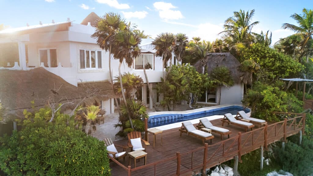 View of Casa Sofia with pool and tropical garden in Tulum, surrounded by palm trees and thatched-roof structures.