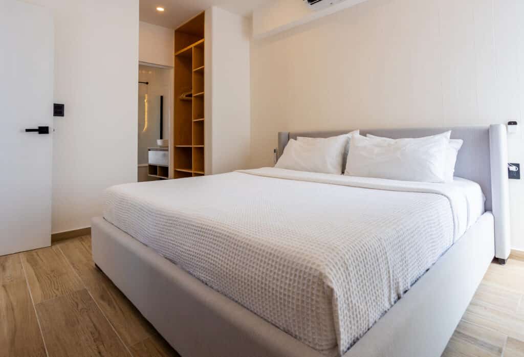 Modern bedroom with white bed, natural wood flooring, and minimal decor at Luna in Playa del Carmen.