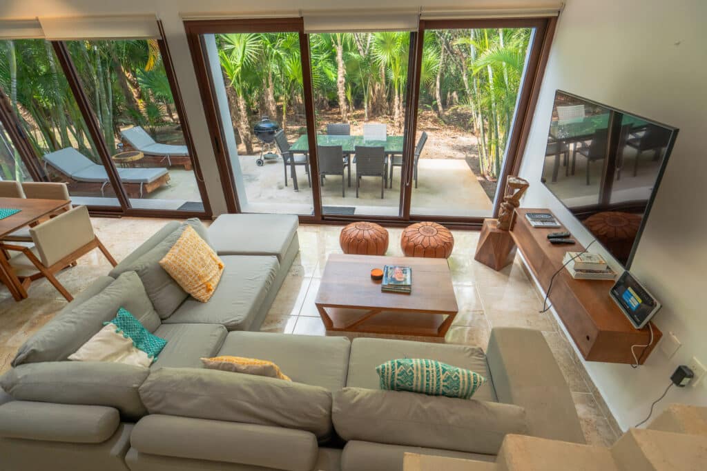 Living room with large glass doors leading to a patio and lush tropical greenery in Akumal.