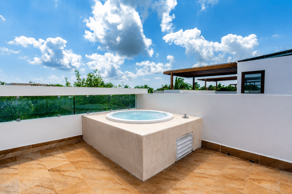Hot tub on a rooftop terrace with a glass railing, overlooking a blue sky with white clouds in Akumal.