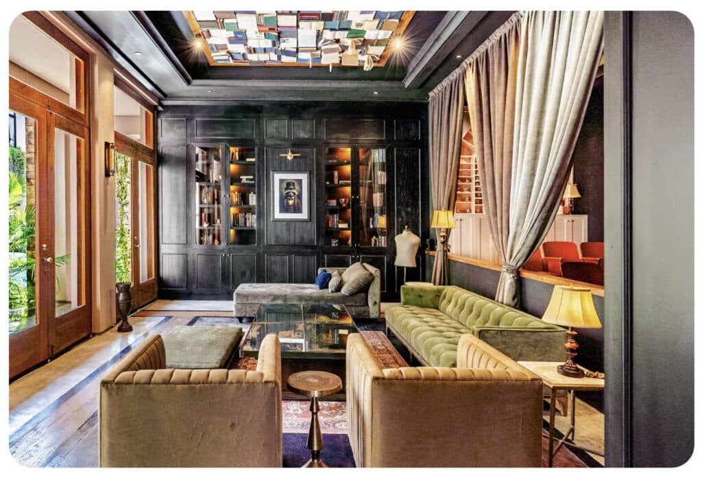 Interior of a sophisticated living room with dark wood paneling, built-in bookshelves, plush seating, and colorful ceiling artwork in Tulum.