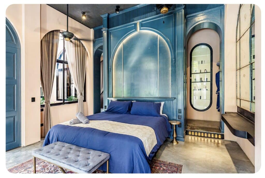 Bedroom with blue paneled walls, large window with curtains, and a bed with blue bedding in a modern apartment in Tulum.