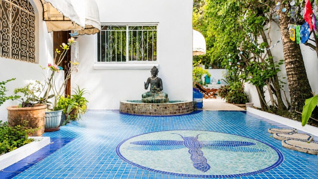 Outdoor patio with a blue mosaic-tiled floor, potted plants, a Buddha fountain, and lush greenery in Playa del Carmen.