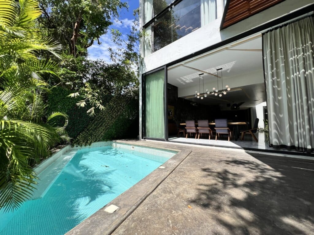 Modern house with an outdoor pool, large glass sliding doors, and lush greenery, located in Playacar at Club Real in Playa del Carmen.