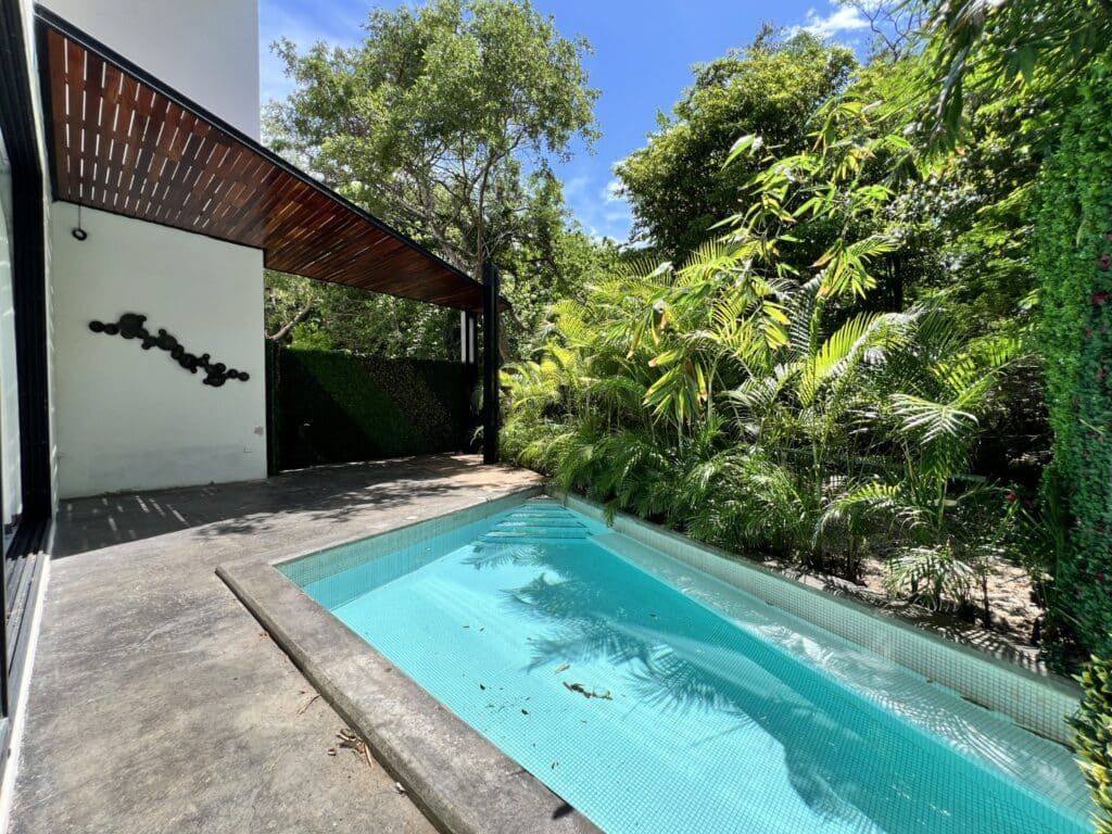 Small private pool surrounded by lush greenery, attached to a modern house at Club Real in Playa del Carmen.