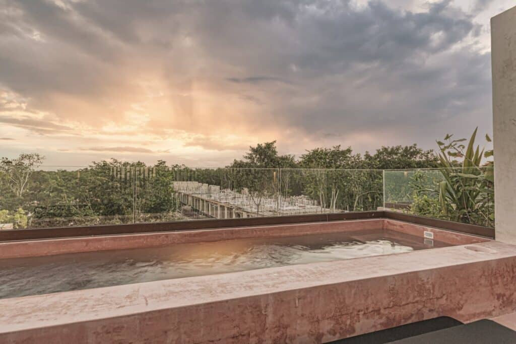 View from a rooftop jacuzzi with trees and sunset in the background in Tulum, Mexico, within Entorno Tulum Villas.