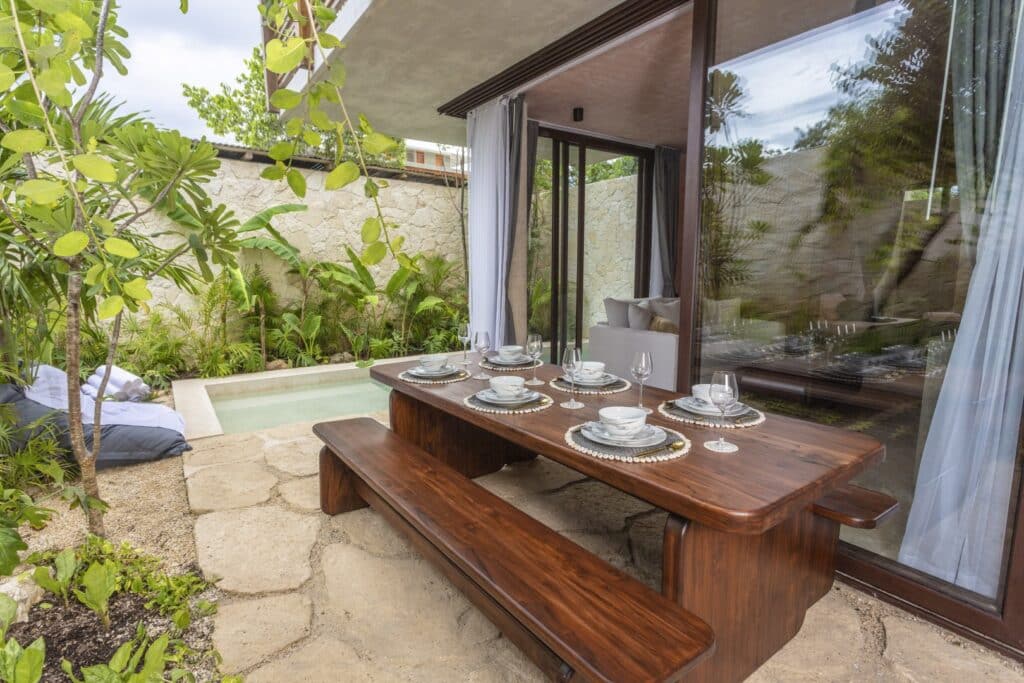 Outdoor dining area with a wooden table and bench, overlooking a small pool and lush garden in Tulum at Entorno Tulum Villas.
